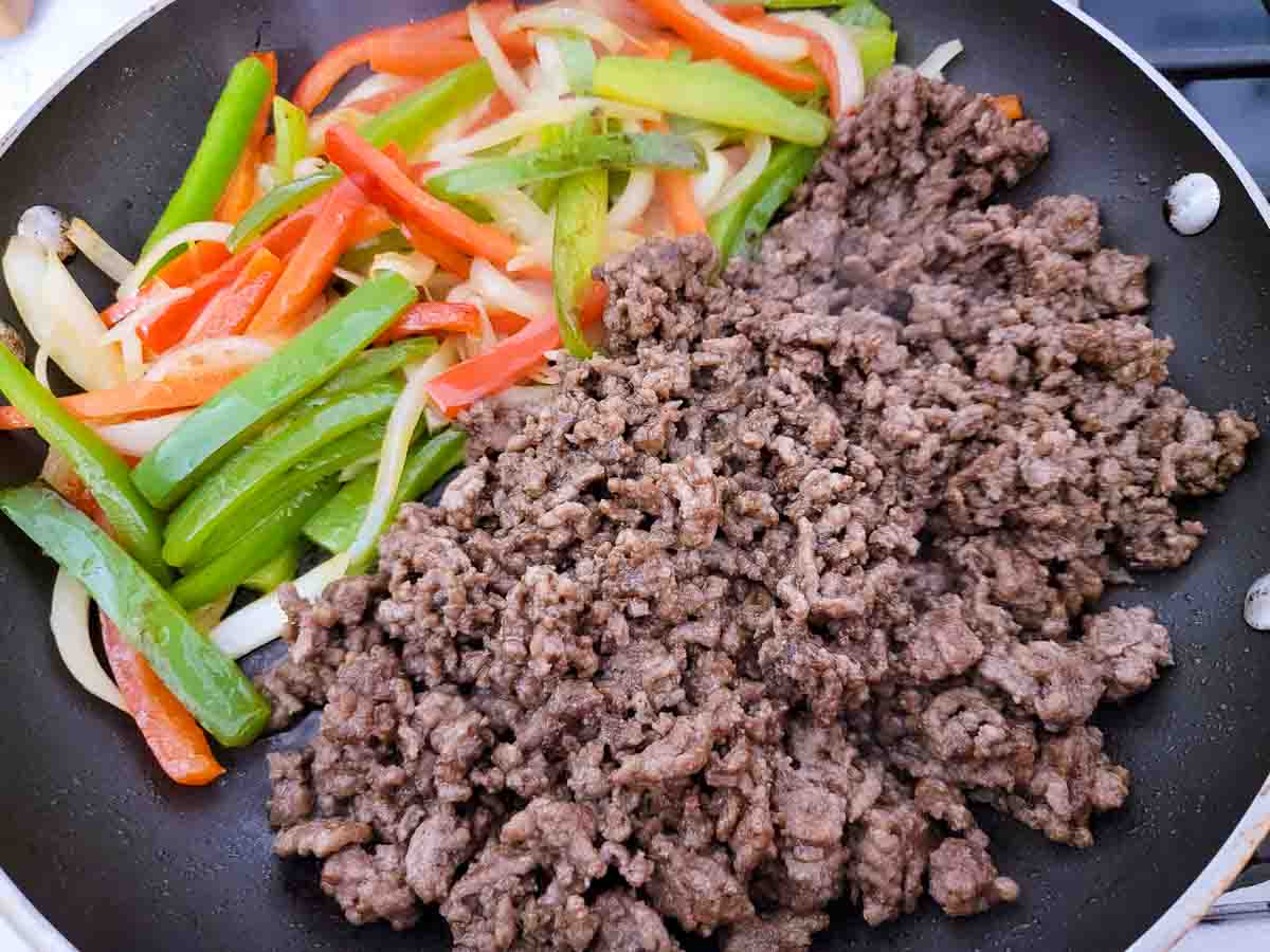 fajita seasoned ground beef, green pepper, red pepper, and onion cooking in a skillet.