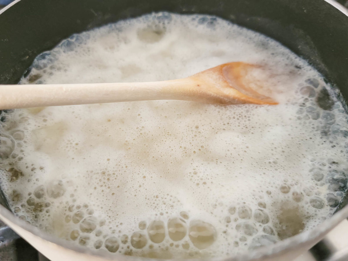 peeled and diced potatoes cooking in a pan with a wooden spoon resting on top of the water.