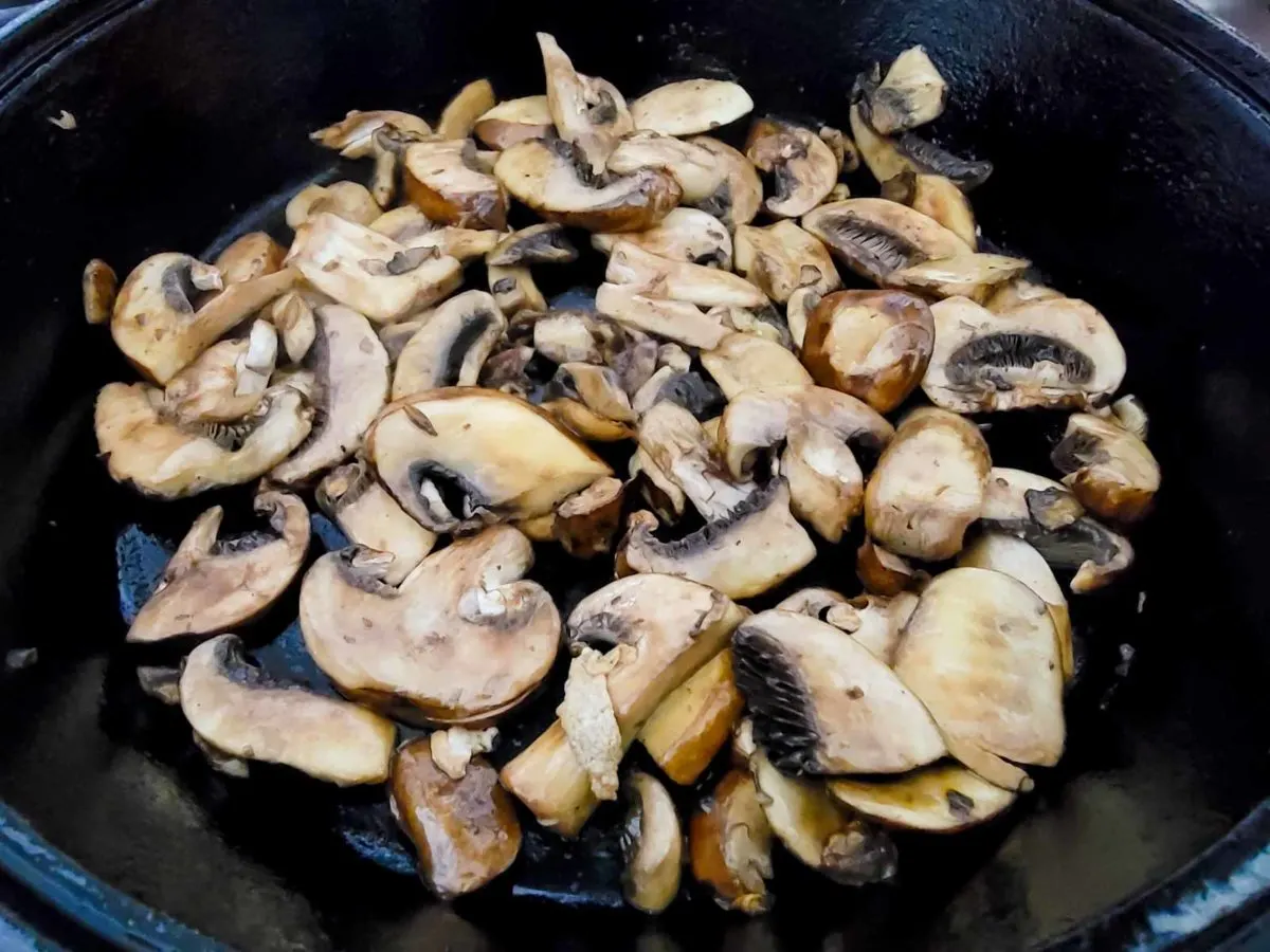 sliced mushrooms cooking in a cast iron skillet.