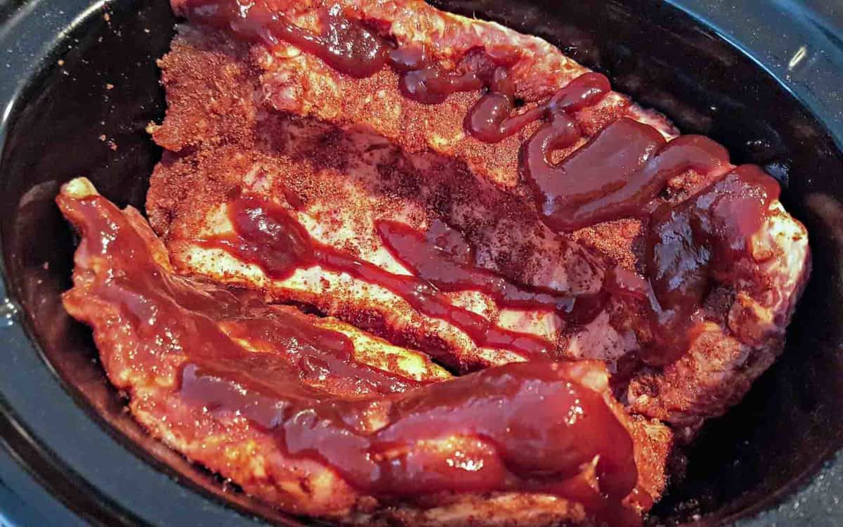 baby back ribs coated in dry rub and bbq sauce in a slow cooker crock pot.