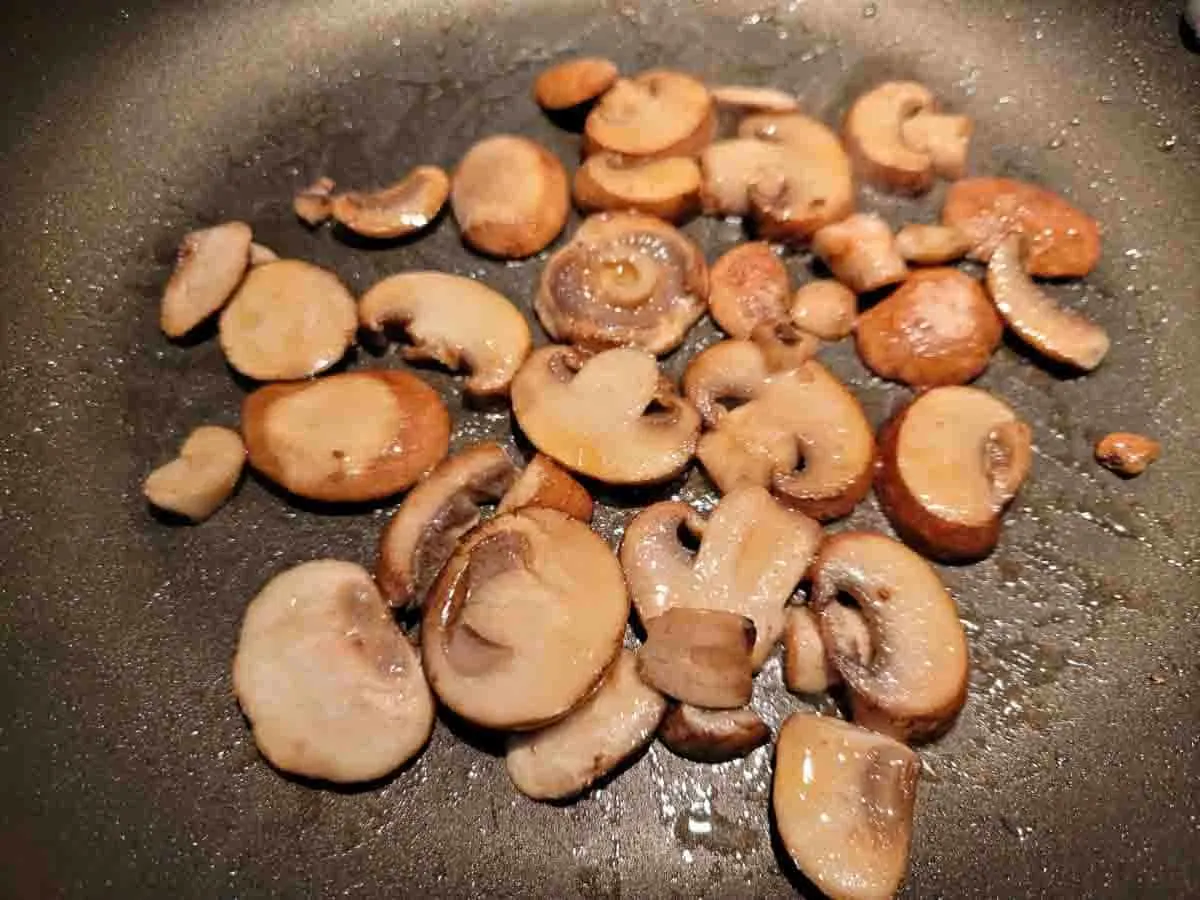 sliced mushrooms cooking in a pan.
