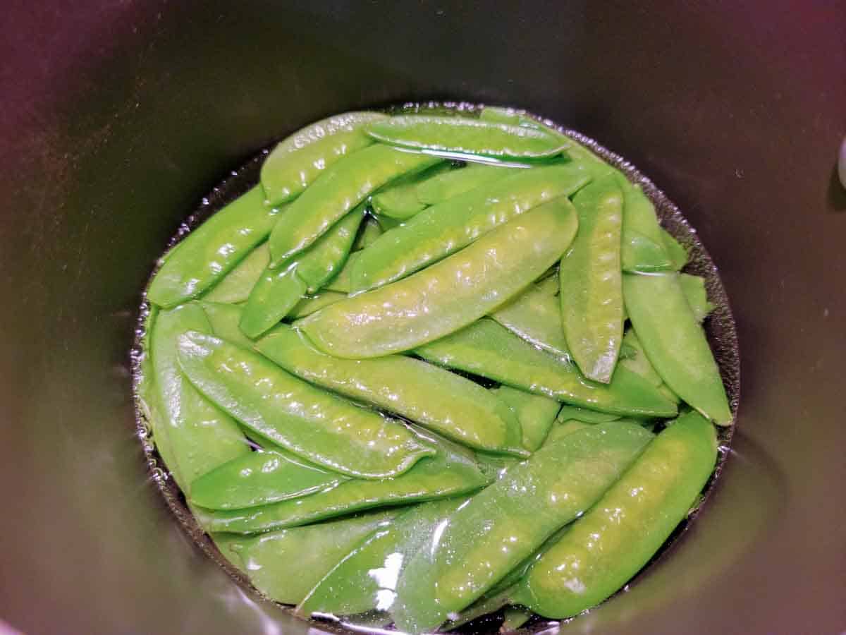 crisp snow peas cooking in a pan of water.