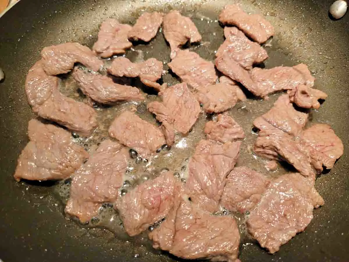 thin sliced beef cooking in a skillet.