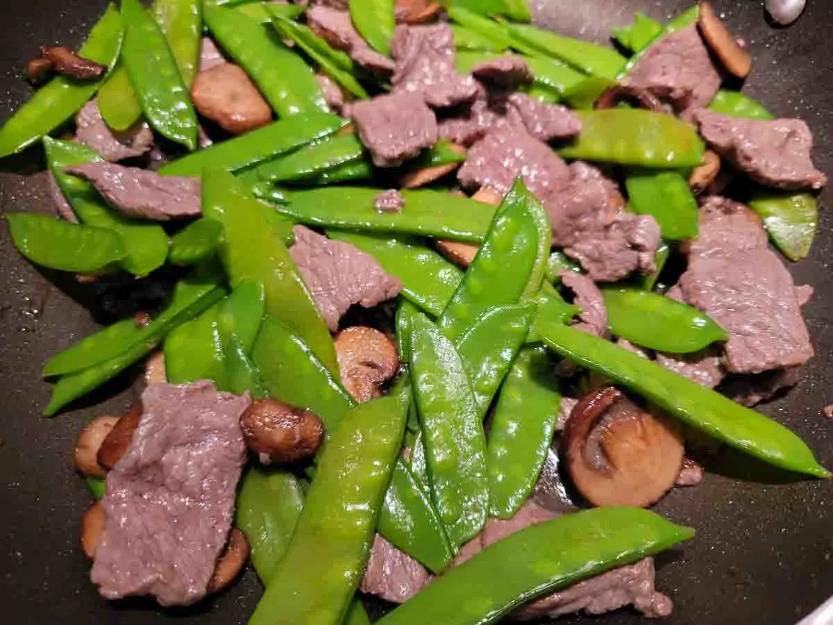 peas, beef, and mushrooms cooking in a pan.