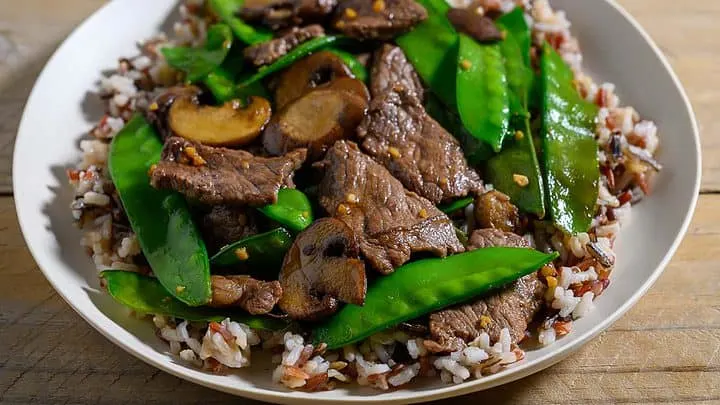 Beef with Snow Peas over rice on a plate.