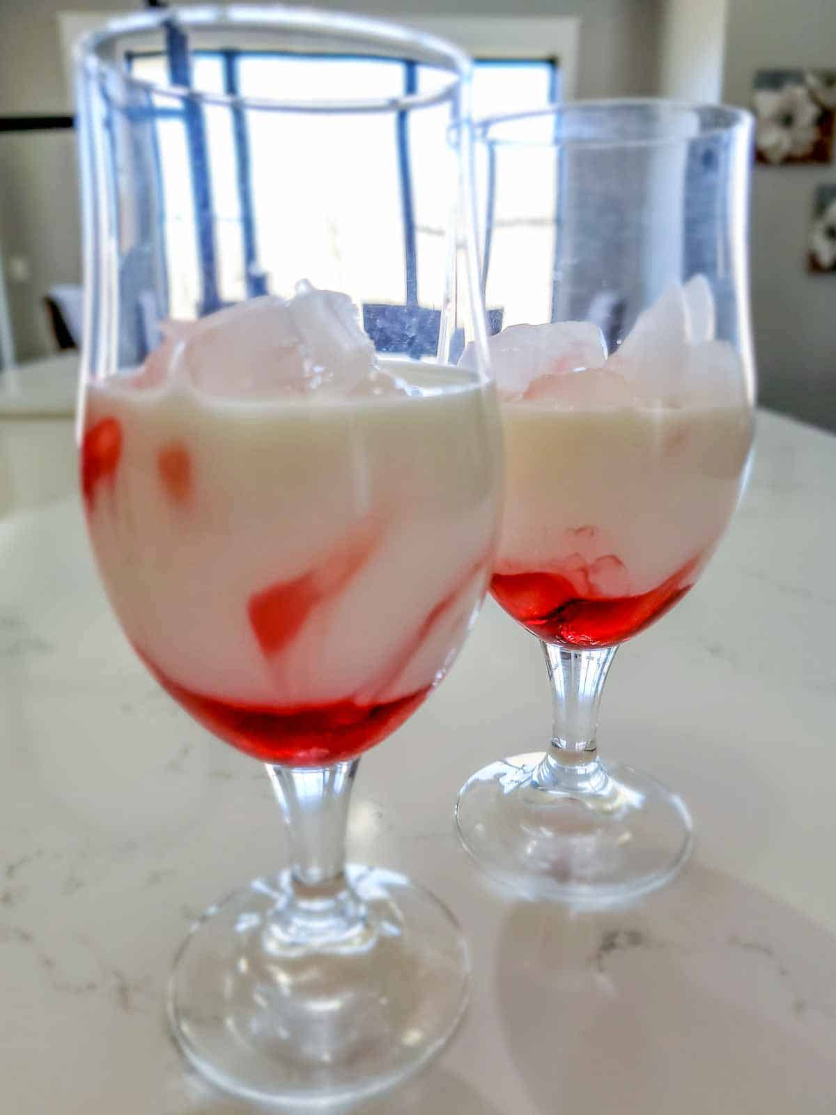 a glass filled with ice, strawberry syrup, and milk.
