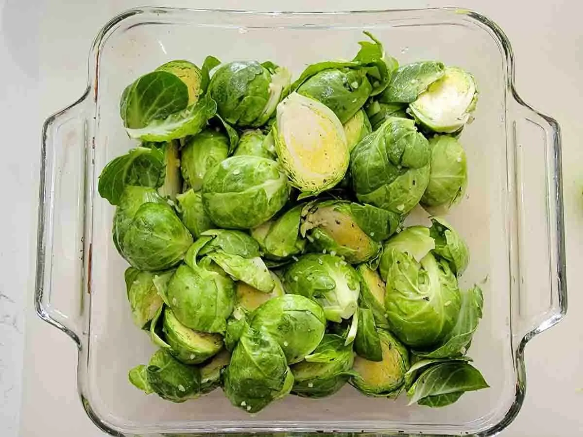 brussels sprouts coated in oil mixture in a baking dish.