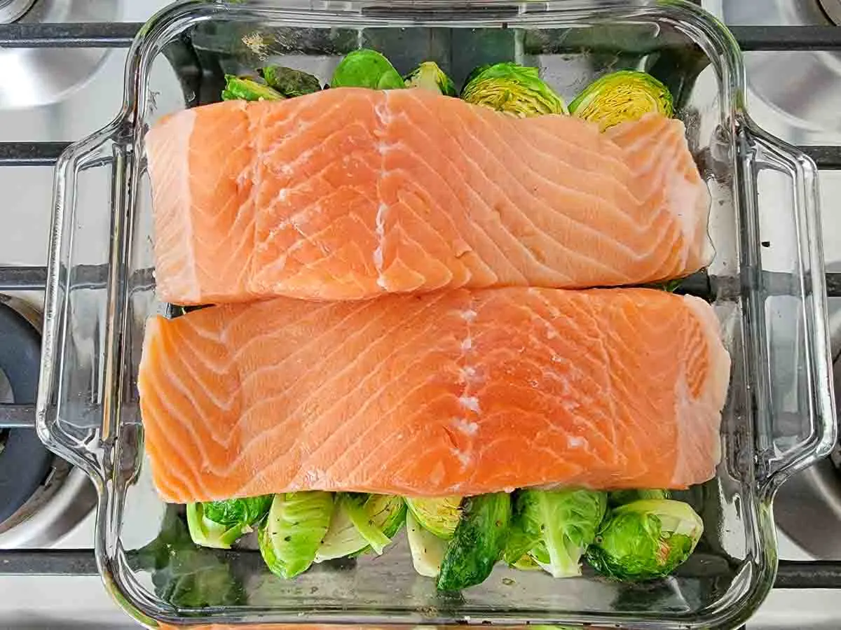 two salmon filets over brussels sprouts coated in oil mixture in a baking dish.