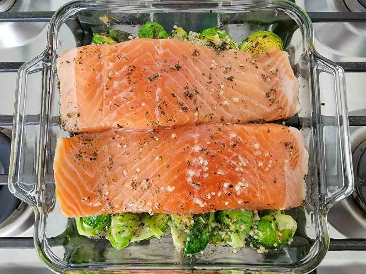 two salmon filets over brussels sprouts topped with oil mixture in a baking dish.