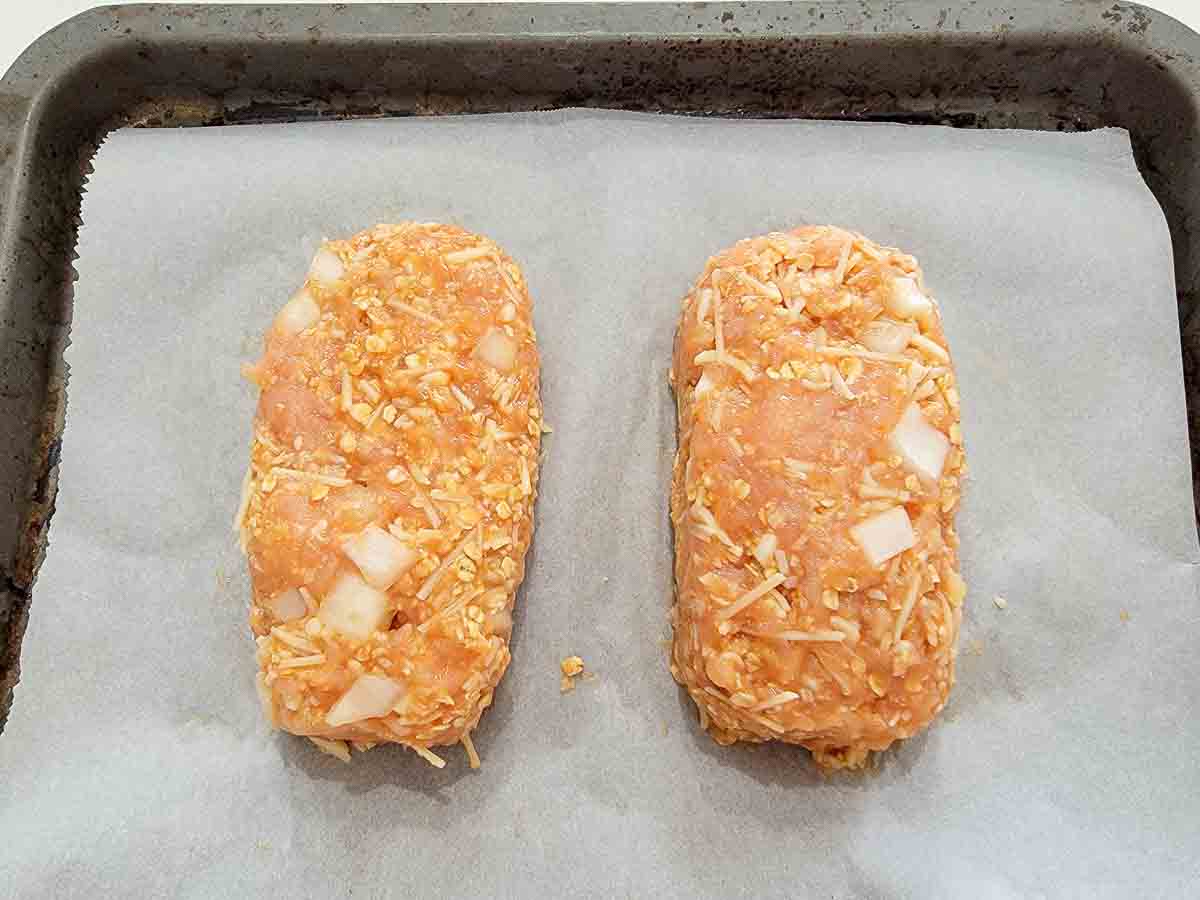 two mini ground chicken meatloaves on a baking sheet.