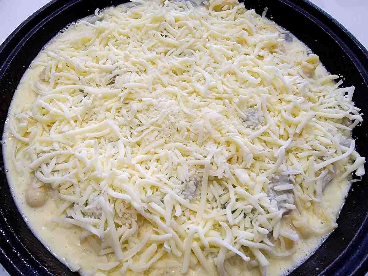 milk mixture, pasta, shrimp, egg, parmesan cheese, and cream cheese mixed in a cast iron skillet.