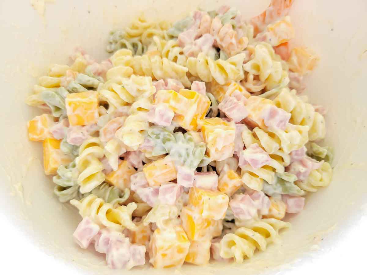 ham, cheddar, rotini pasta, and mayo mixed in a bowl.