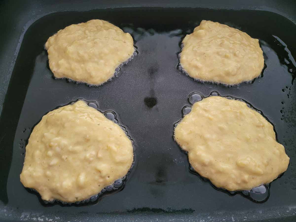 4 banana pancakes cooking in a skillet.