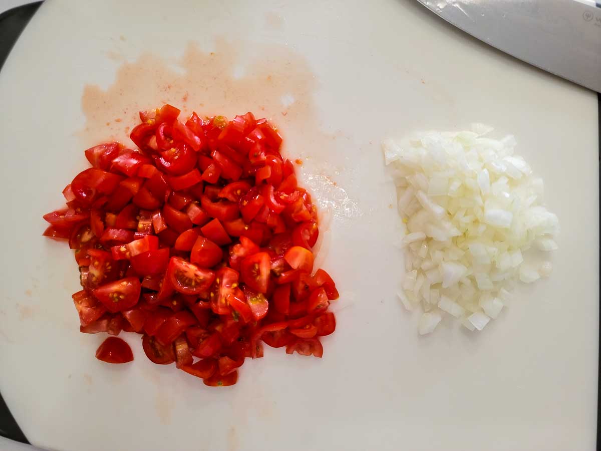 cherry tomatoes and onions diced on a cutting board.