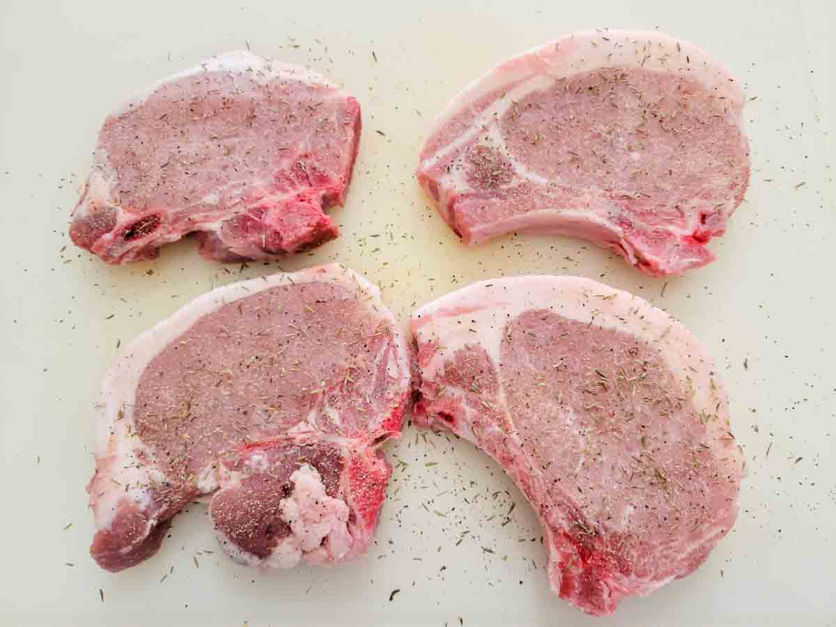four pork chops topped with herbs and seasonings.