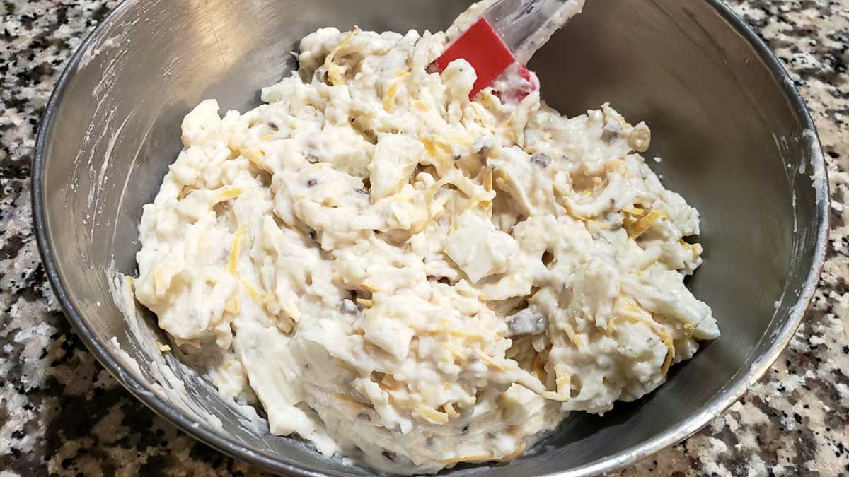 soup and sour cream, and cheddar cheese added to hash browns, melted butter, salt, and pepper in a bowl.