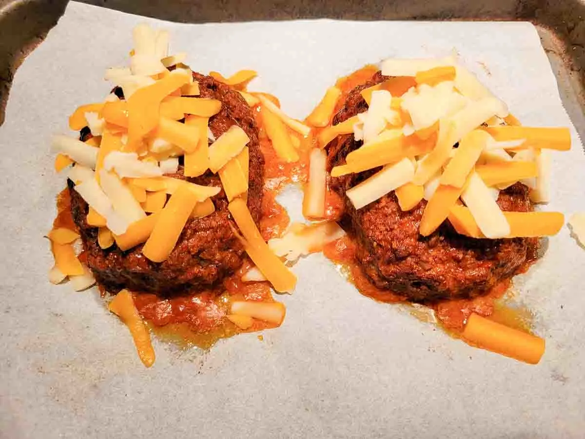 two baked taco meatloaves topped with shredded cheese on a baking sheet.