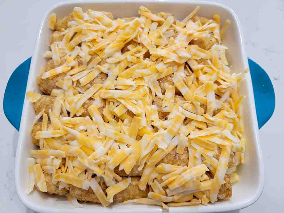 shredded cheese. tater tots, cream of mushroom soup, mixed vegetables and rotisserie chicken in a casserole dish.