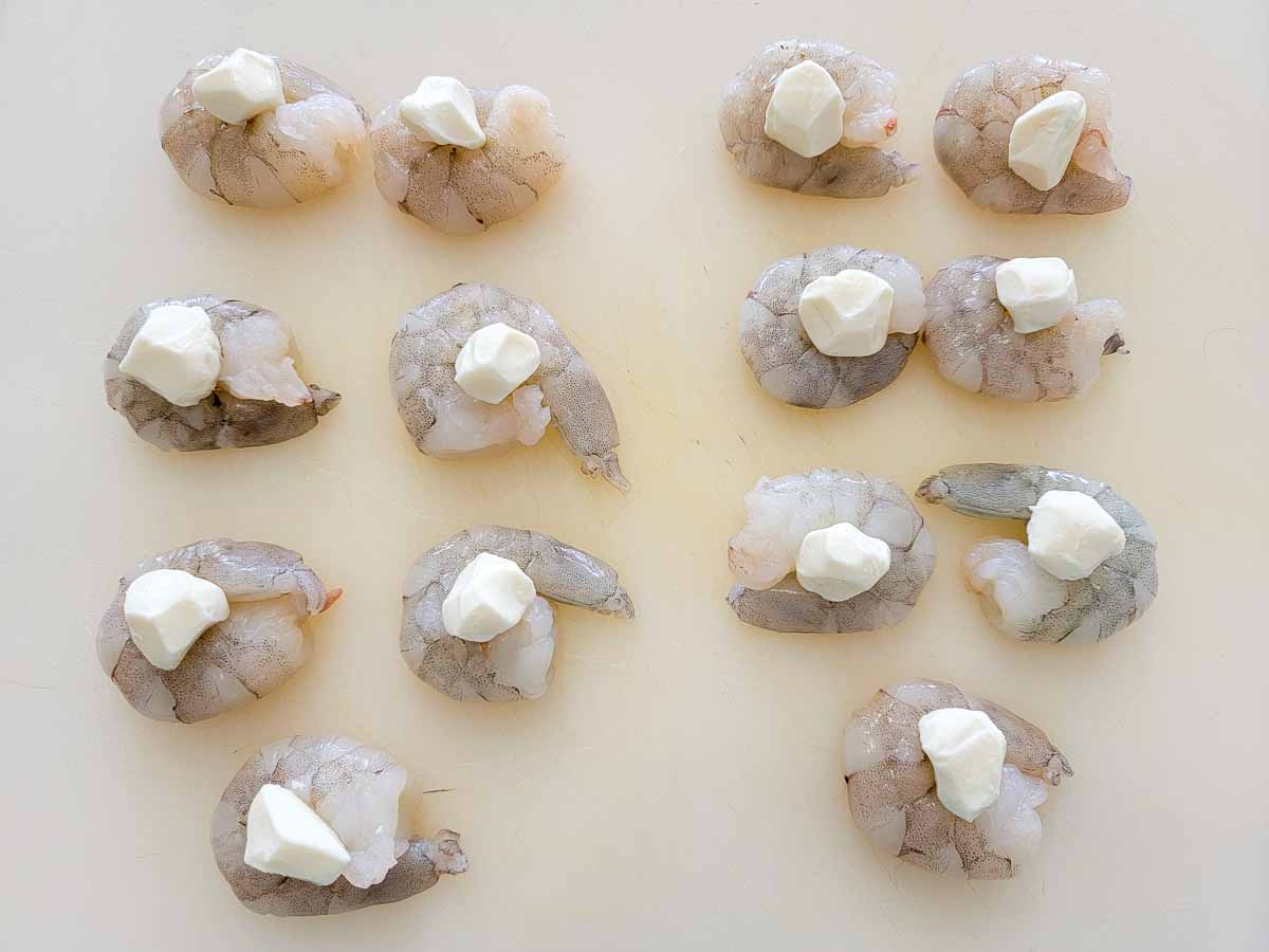 raw shrimp topped with a mozzarella ball on a cutting board.