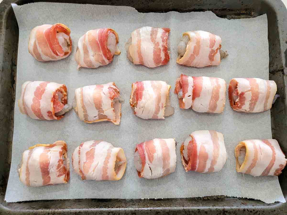 raw shrimp topped with a mozzarella ball and wrapped in a slice of bacon on a cutting board.