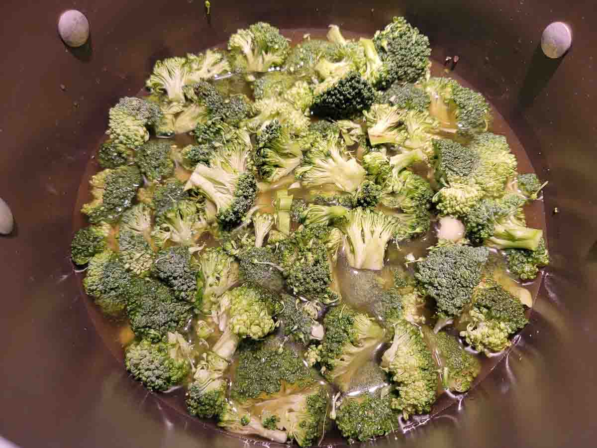 chicken broth, chopped broccoli, and onion powder cooking in a pan.