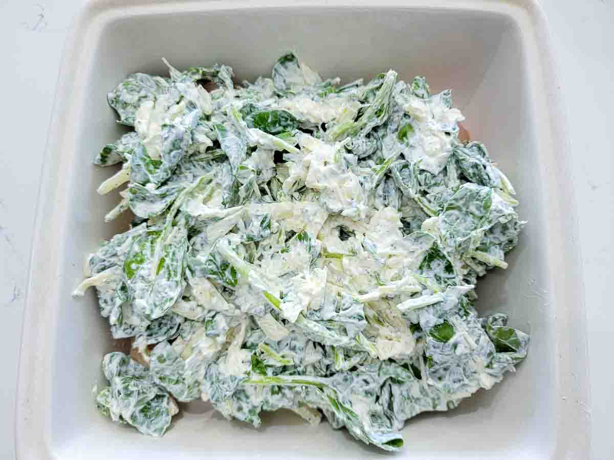 chicken breasts topped with baby spinach leaves, mozzarella, sour cream, Parmesan, oregano, basil, garlic powder, salt and pepper in a casserole dish.