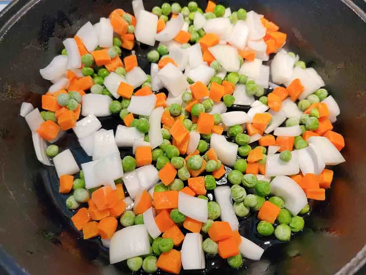 peas, carrots, and onions cooking in a cast iron skillet.