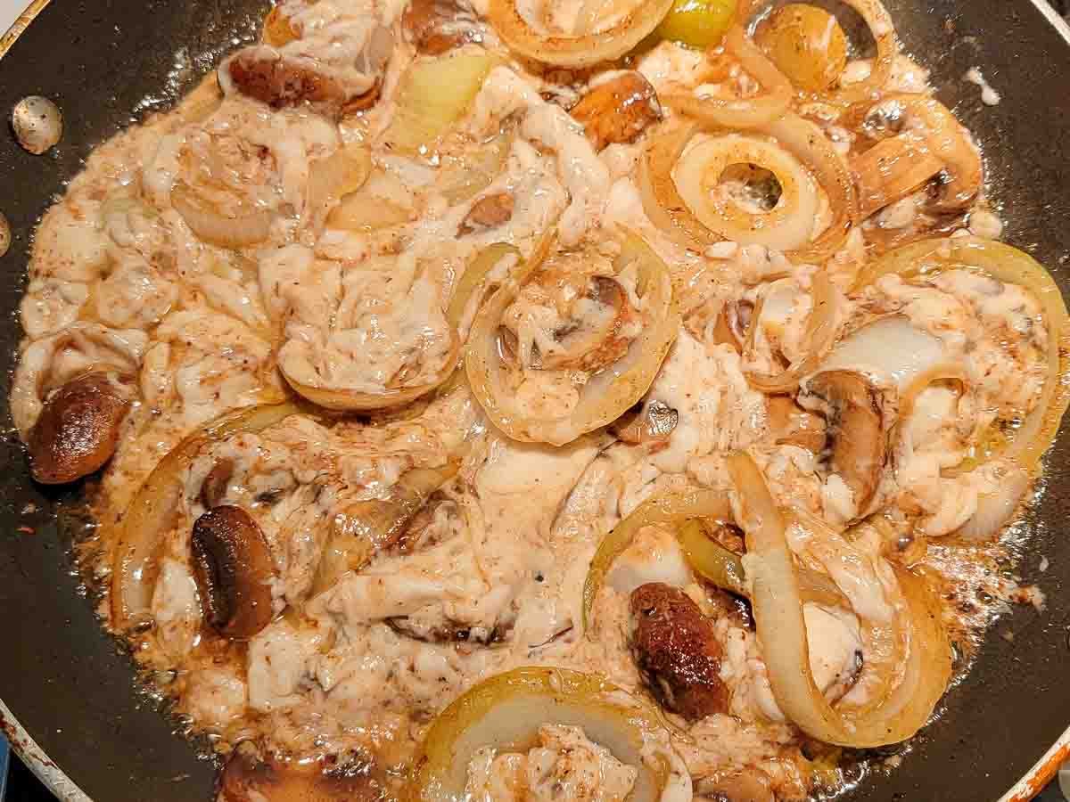 garlic, cream of mushroom soup, onion slices and mushroom slices cooking in a pan.
