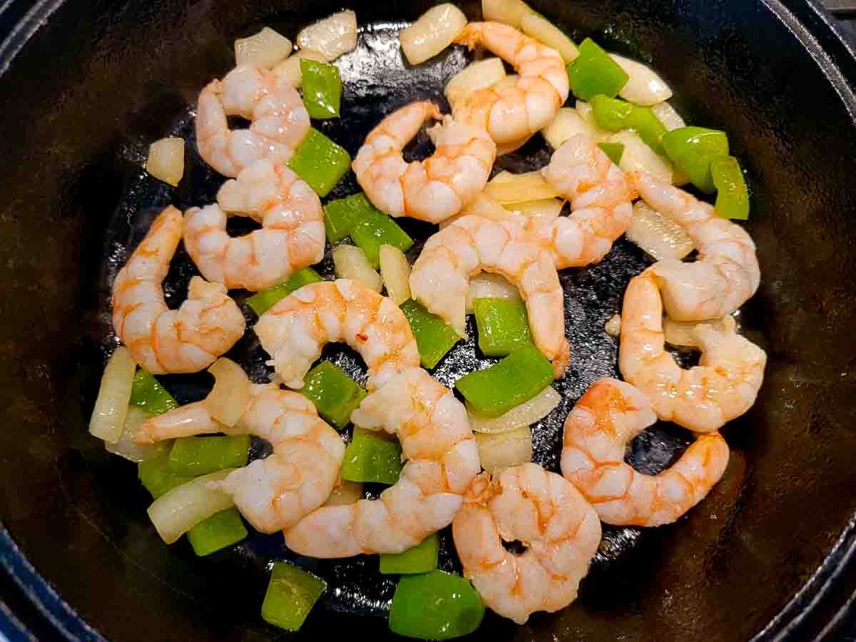 shrimp, green pepper and onion frying in a skillet.