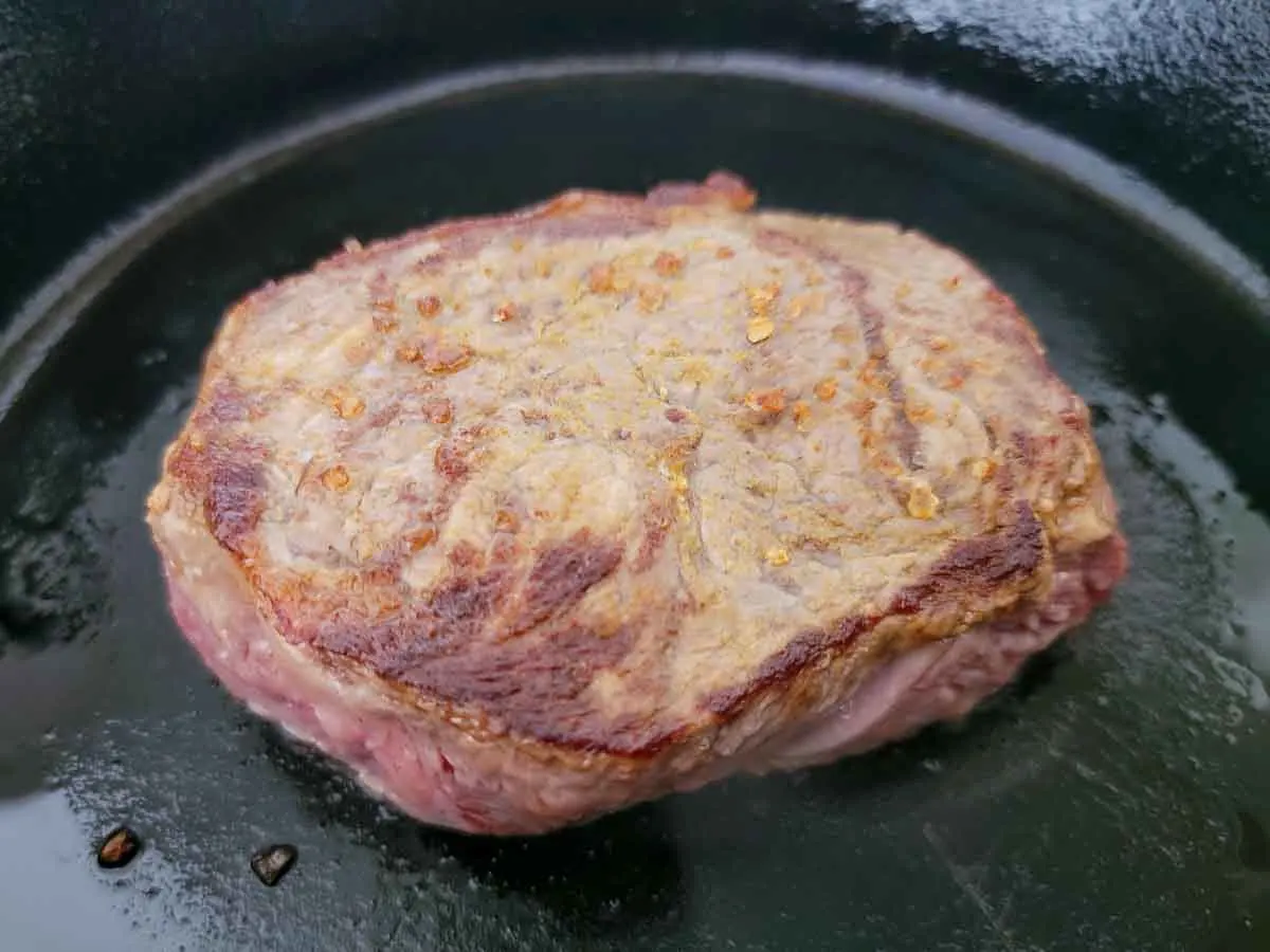 beef tenderloin steak sprinkled with salt and cumin frying in a cast iron skillet.