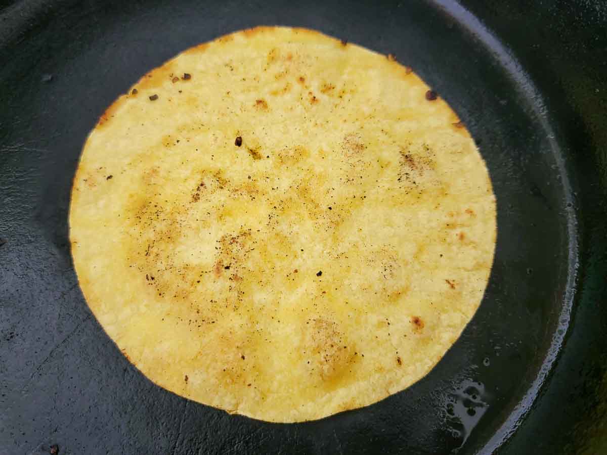 a corn tortilla frying in a skillet.