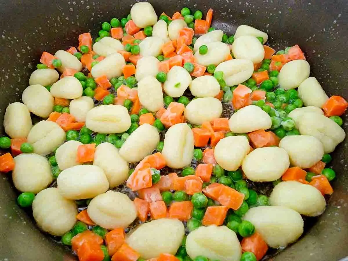 butter, gnocchi, peas, salt, pepper, and carrots cooking in a pan.