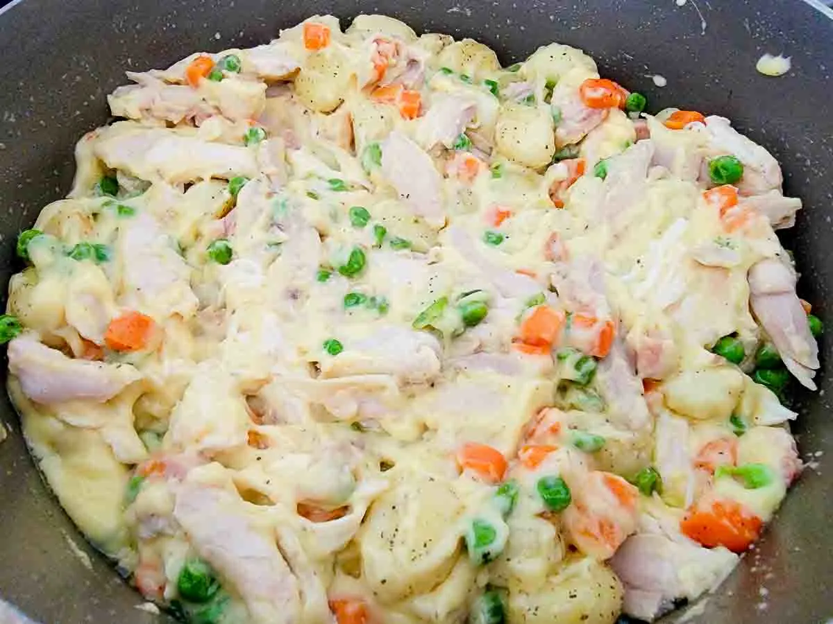 cream of chicken soup, shredded chicken, butter, gnocchi, peas, salt, pepper, and carrots cooking in a pan.