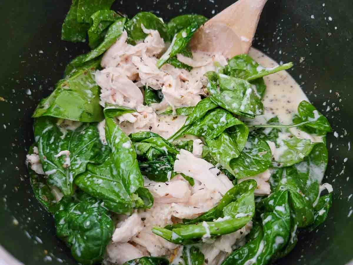 spinach, shredded chicken, chicken broth, heavy cream, butter, garlic, salt, pepper, onion powder, and Italian seasoning cooking in a pan.