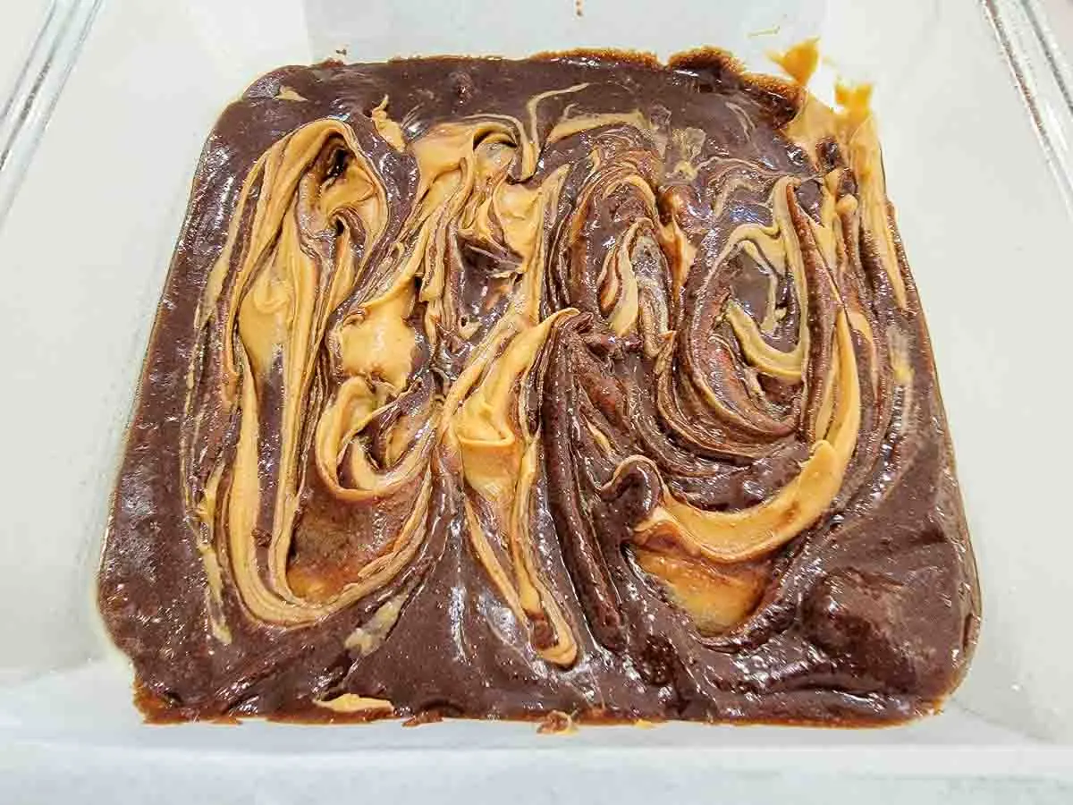 peanut butter swirled on top of brownie batter in a square baking dish.