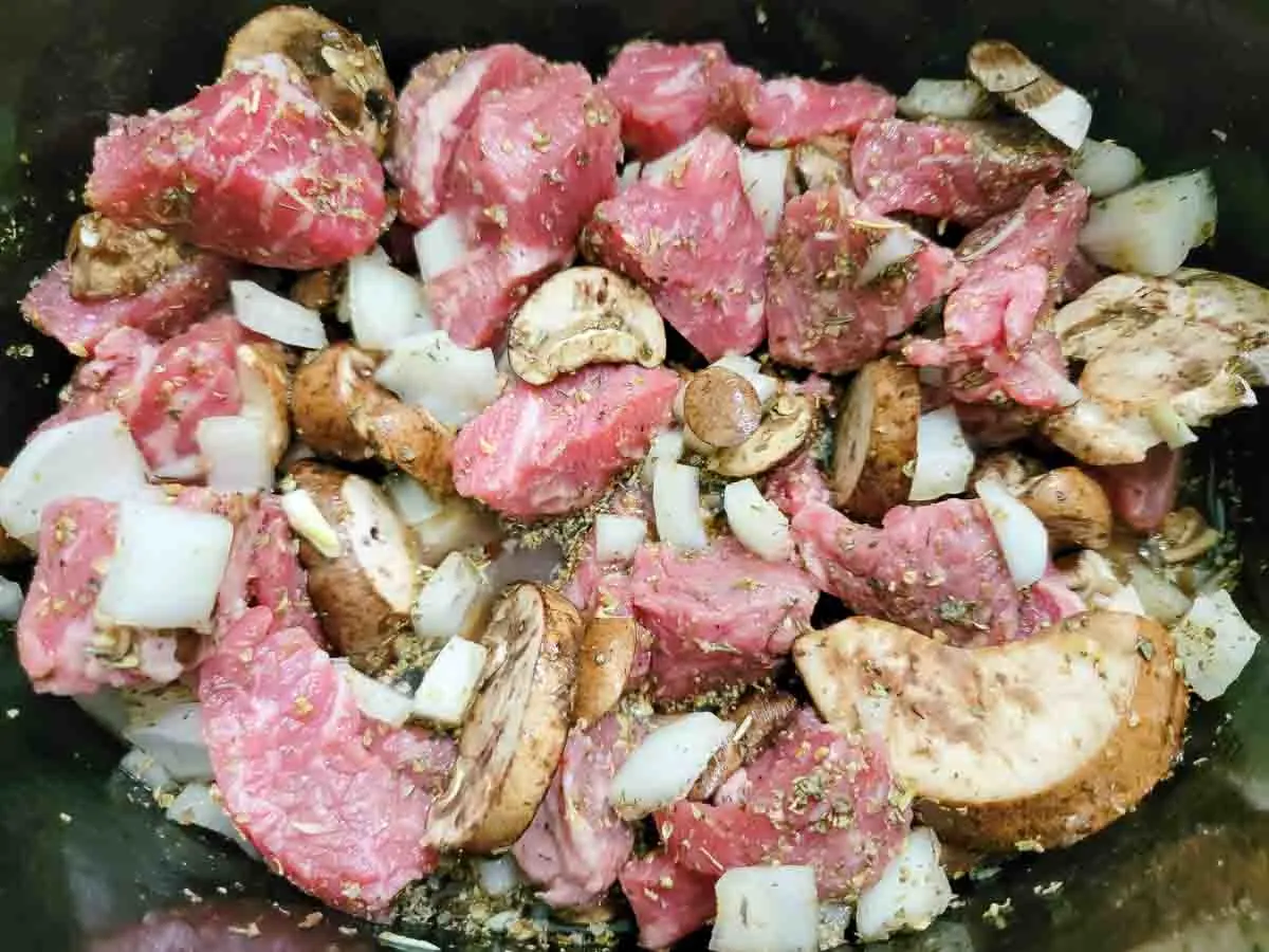 beef, onions, garlic, beef broth, mushrooms, and Italian seasoning in a crockpot.