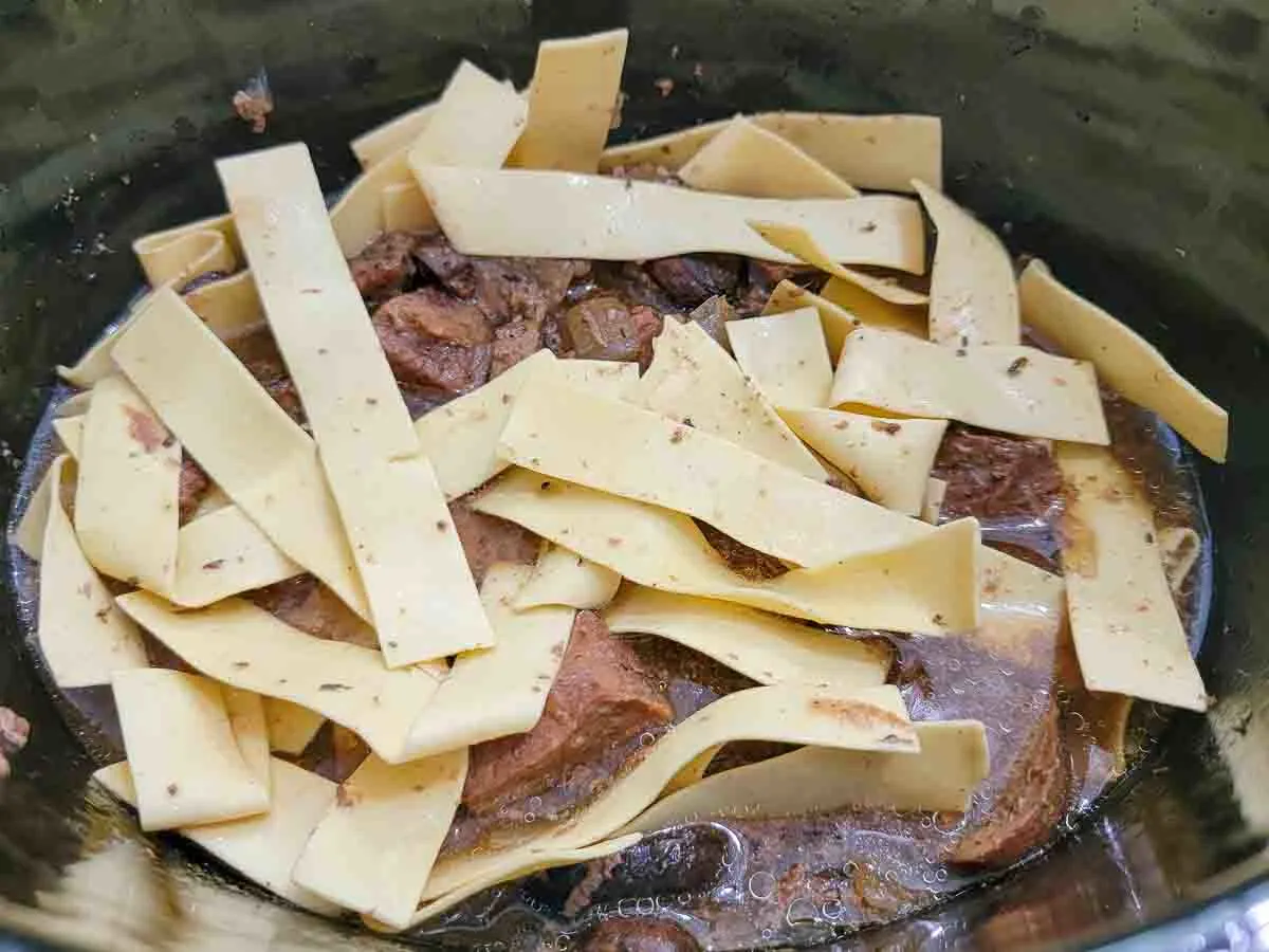 long flat pasta, beef, onions, garlic, beef broth, mushrooms, and Italian seasoning in a crockpot.