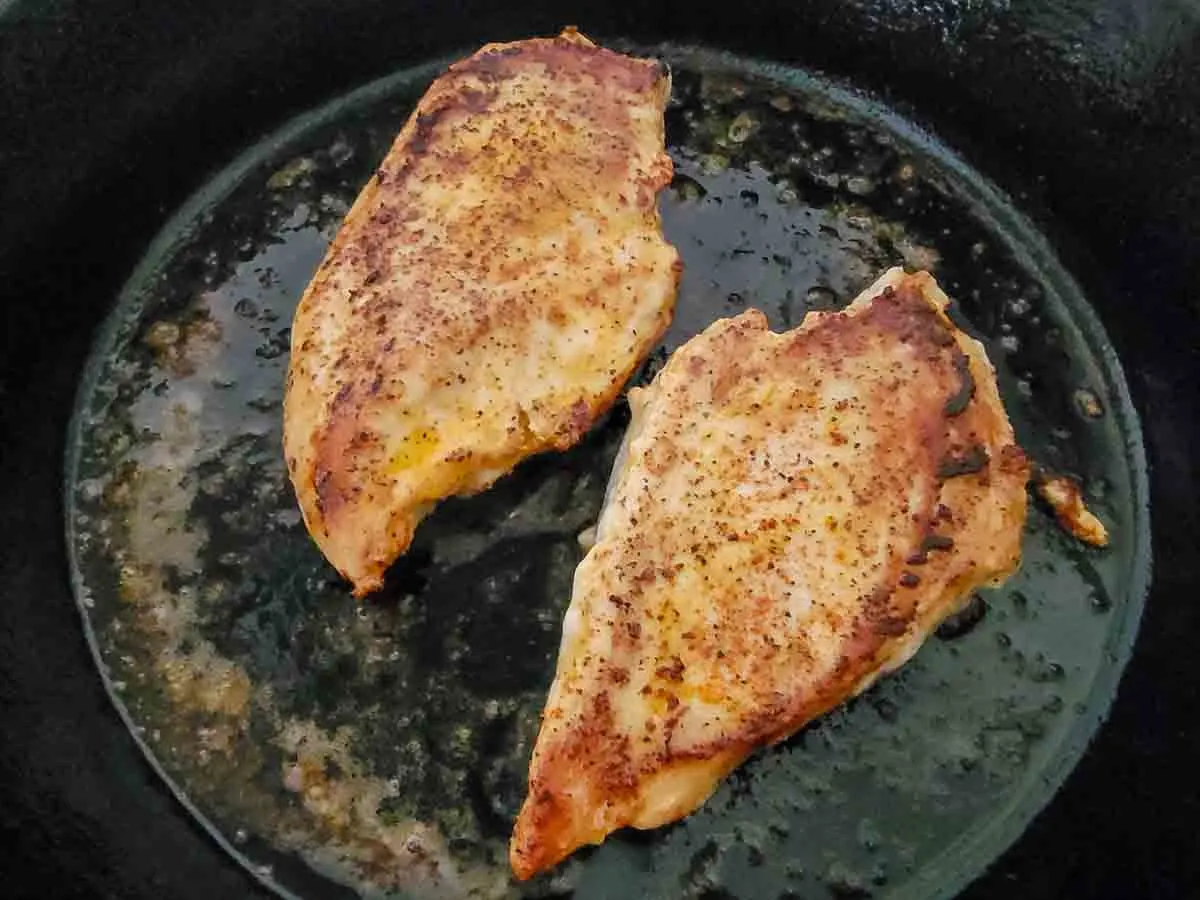 two boneless chicken breasts frying in a pan.