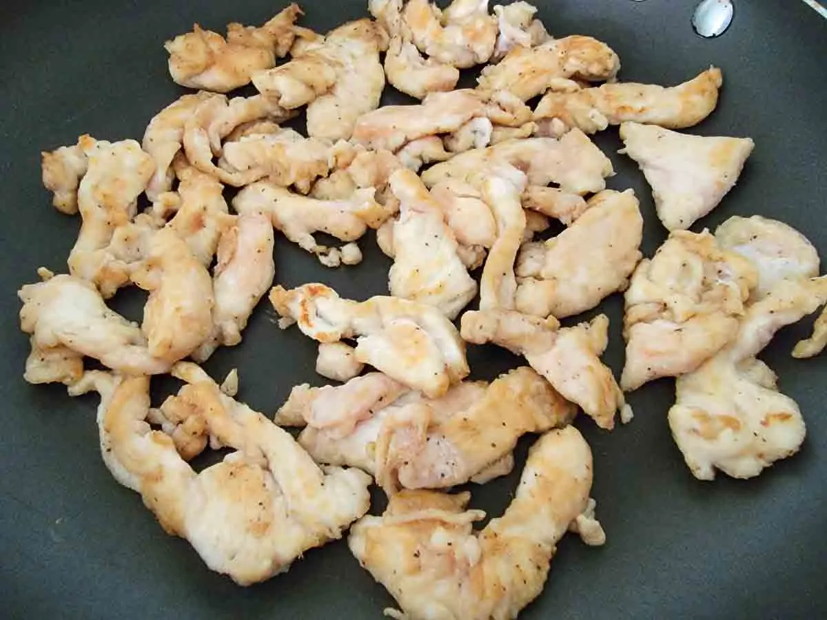 sliced chicken frying in a pan.