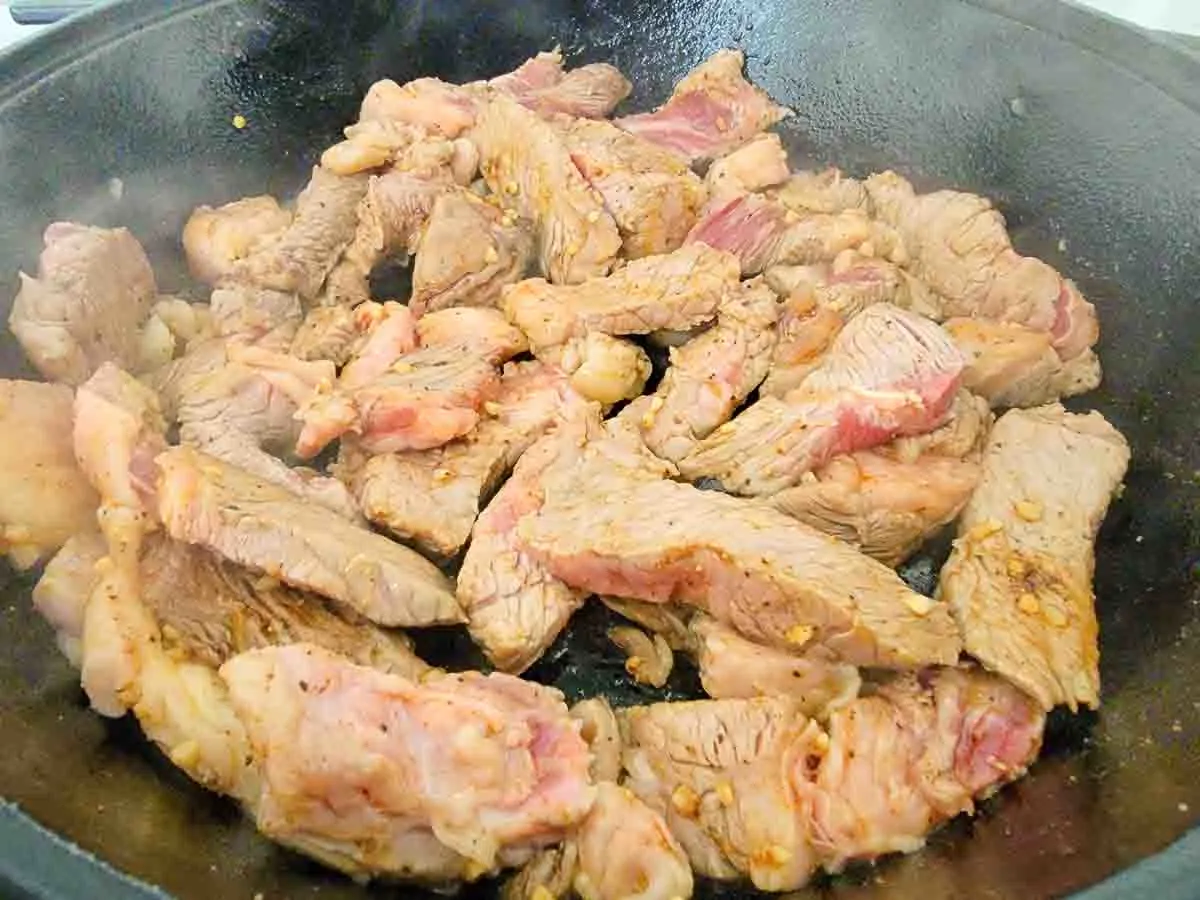 sliced ribeye steak cooking in a skillet.