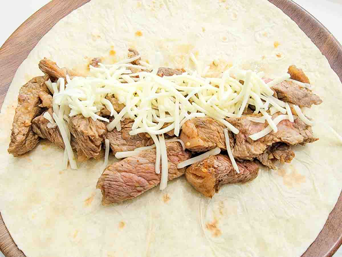 sliced ribeye steak and shredded cheese layered on a large tortilla.