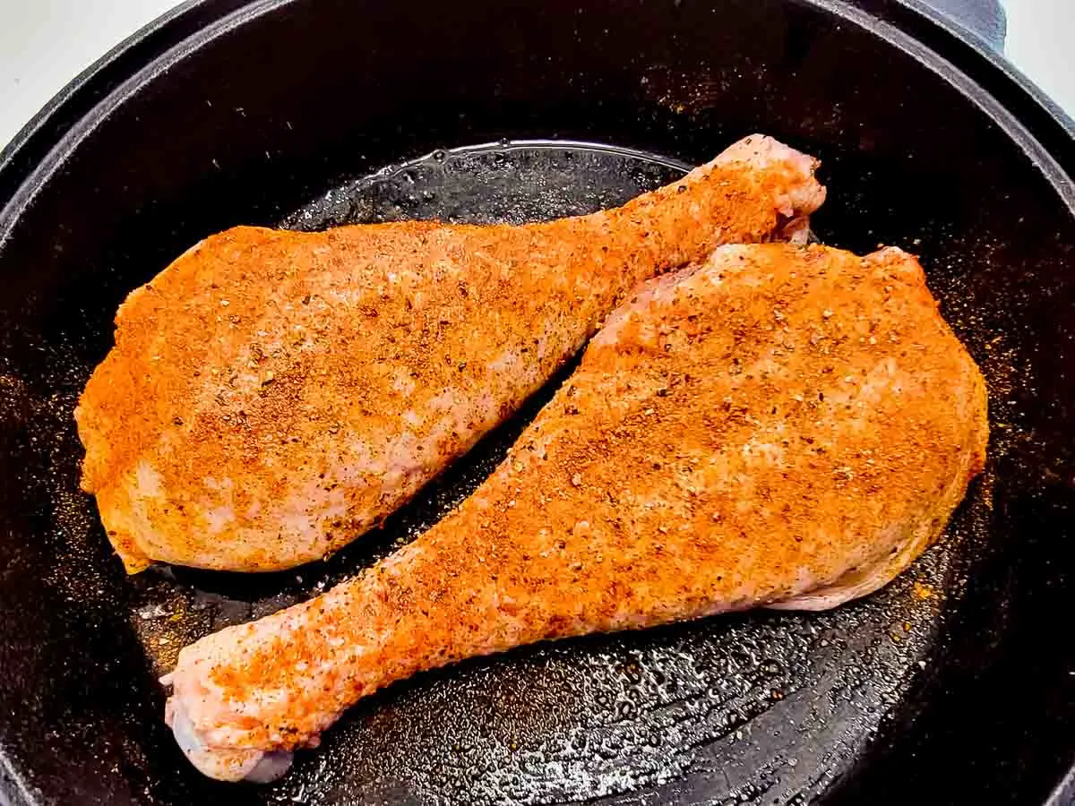 two turkey drumsticks seasoned with rotisserie chicken seasoning in a cast iron skillet.