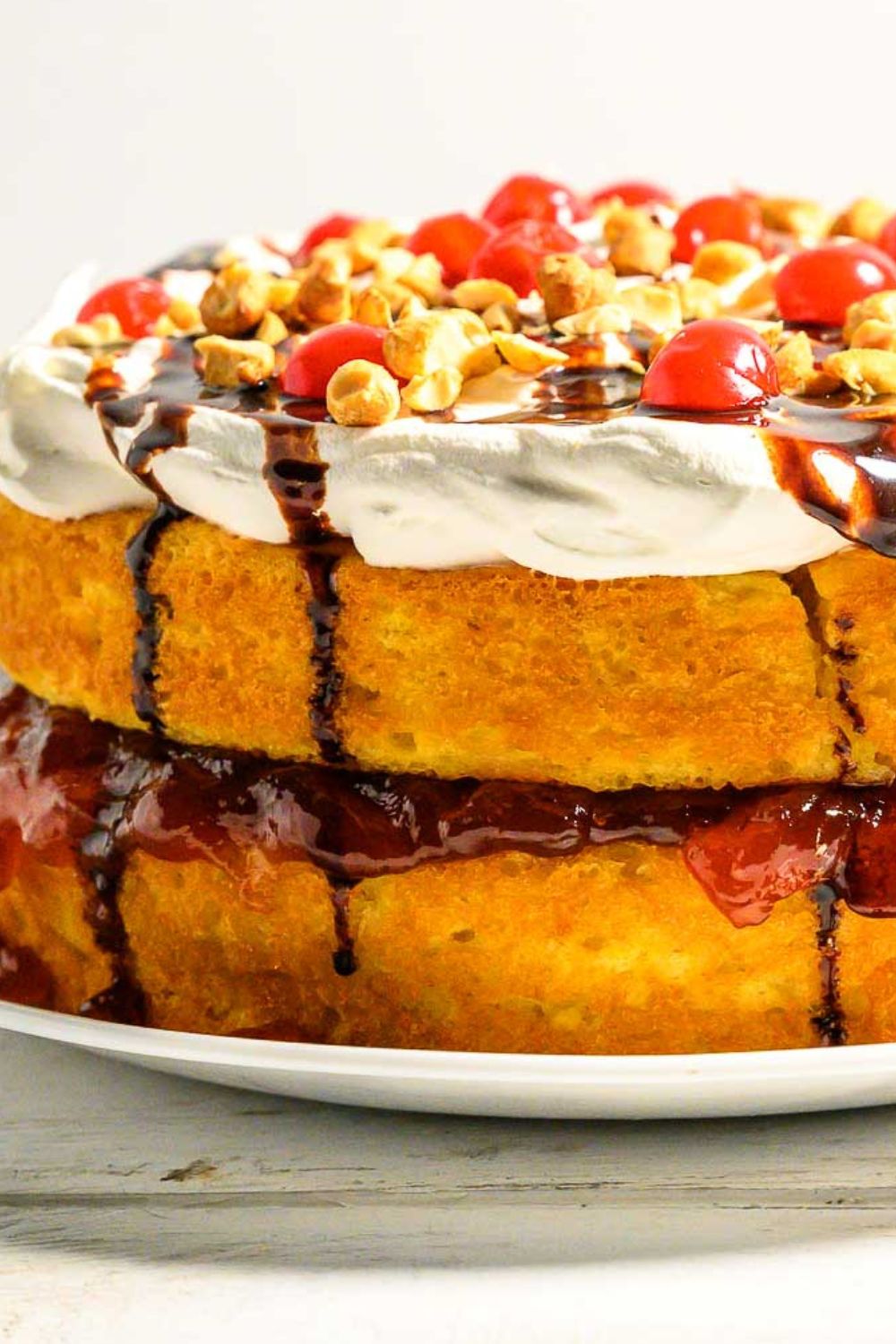 a cake with layers of yellow cake mix, banana pudding, crushed pineapple, strawberry jam, cool whip, chocolate syrup, and maraschino cherries.