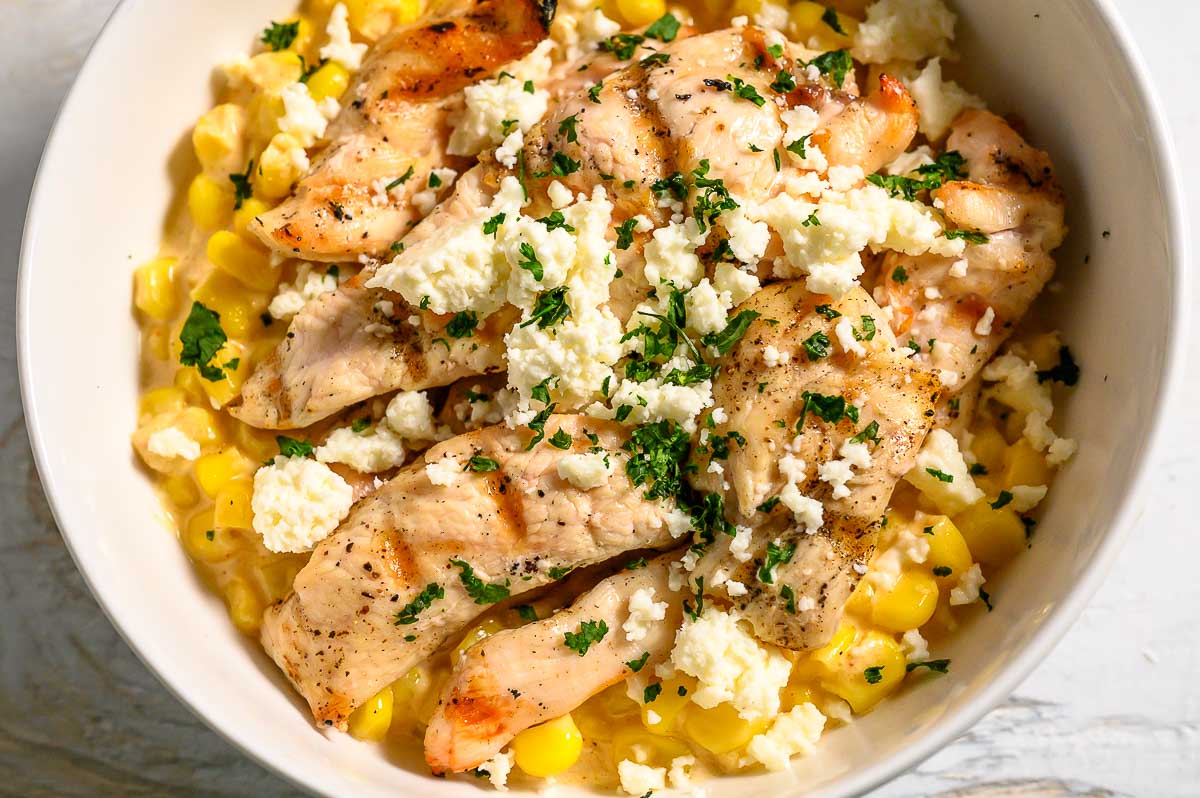 a bowl filled with corn, chicken, cheese, mayo sauce, and seasonings.