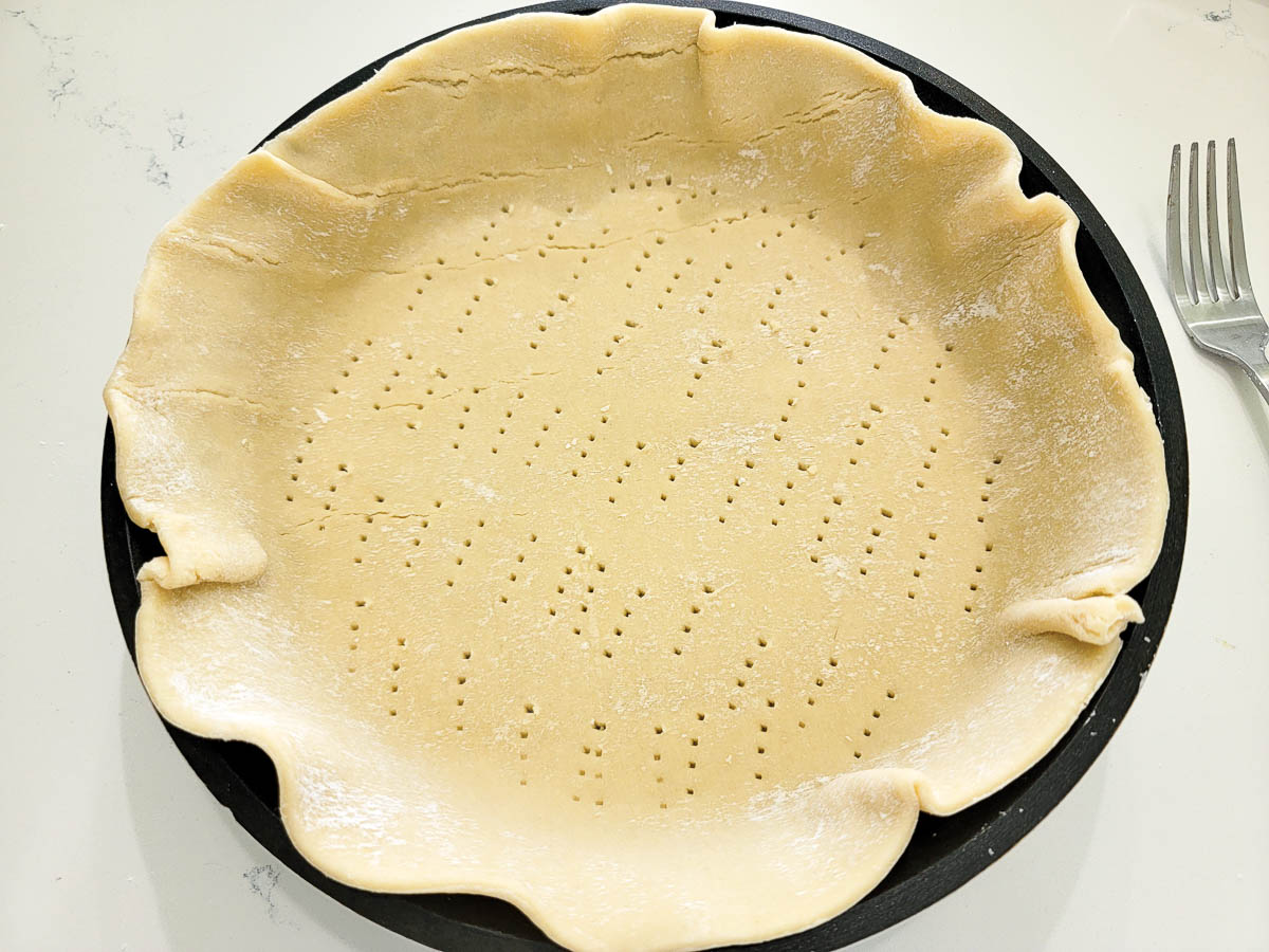 unbaked pie crust poked with fork holes in a pie pan.