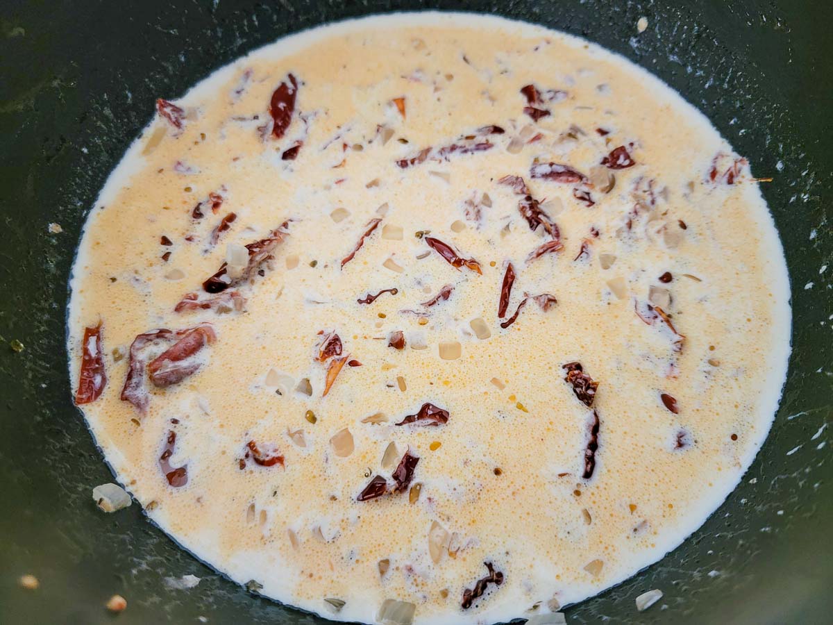 heavy cream, butter, minced garlic, onions, and sun-dried tomatoes cooking in a frying pan.