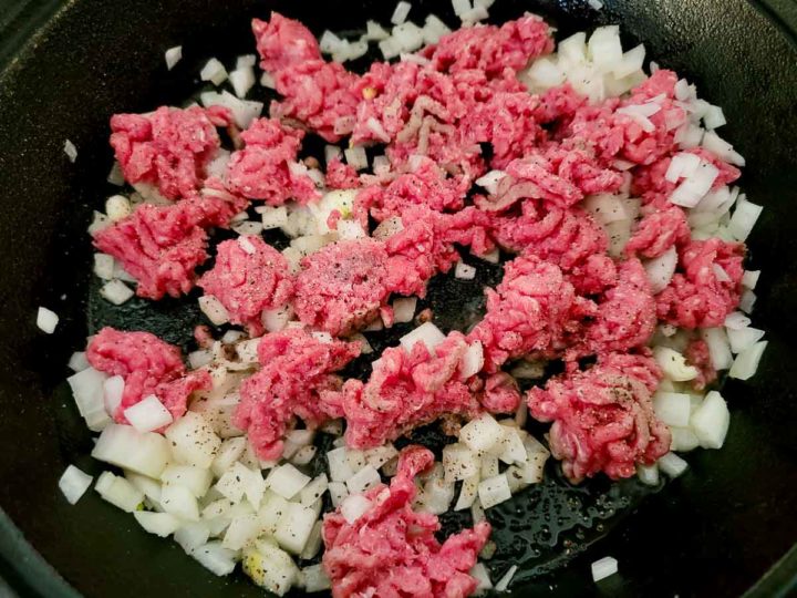 ground beef, onions, salt, and pepper cooking in a cast iron skillet.