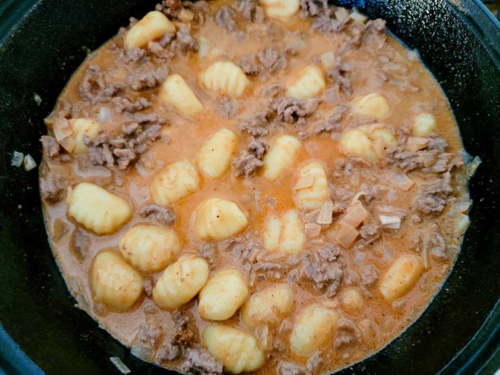ground beef, onions, salt, garlic powder, paprika, chili powder, tomato paste, Worcestershire sauce, heavy cream, beef broth, gnocchi, and pepper cooking in a cast iron skillet.