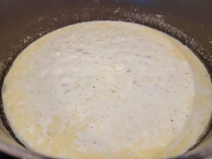 butter, cream cheese, milk, Parmesan cheese, jarred minced garlic, salt, and pepper cooking in a pan.