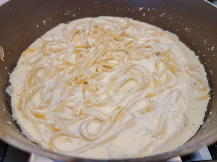 long flat pasta cooking in a white cream sauce.